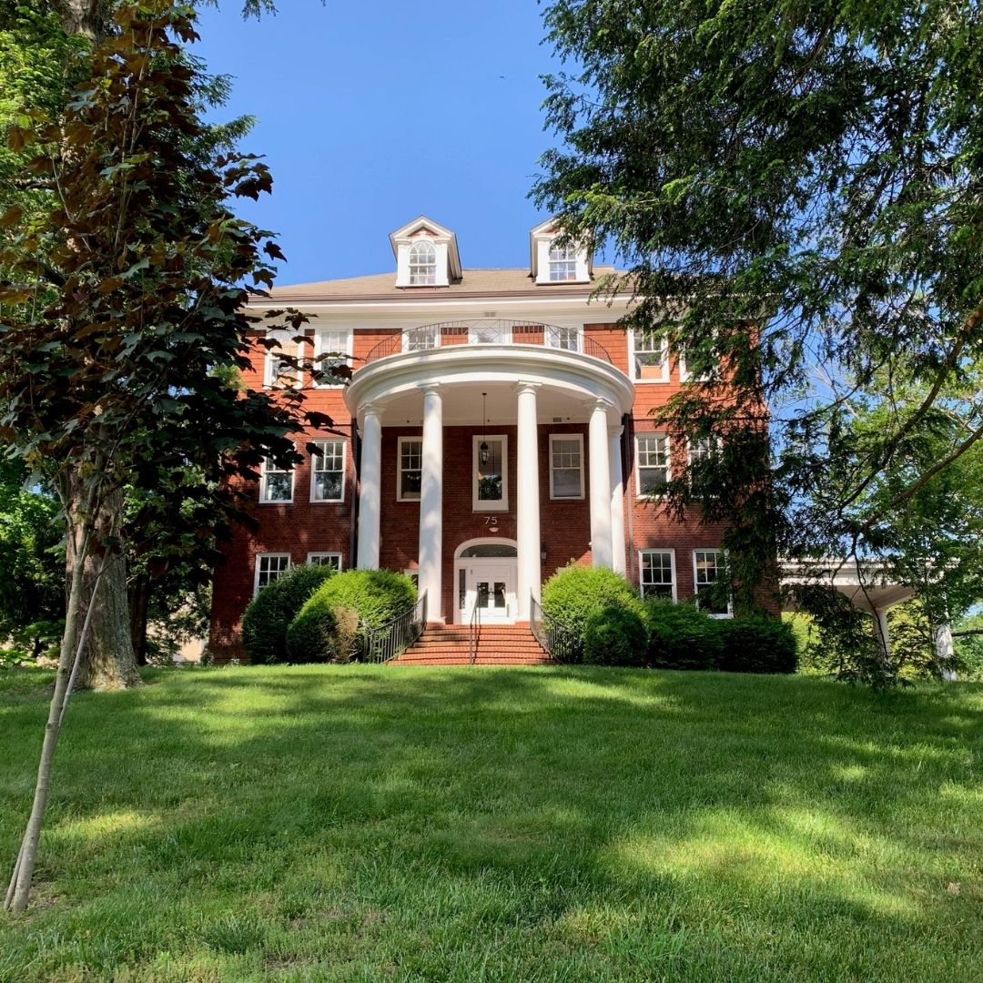 The Goodale School's red brick building with white pillars along the front and flanked by trees.