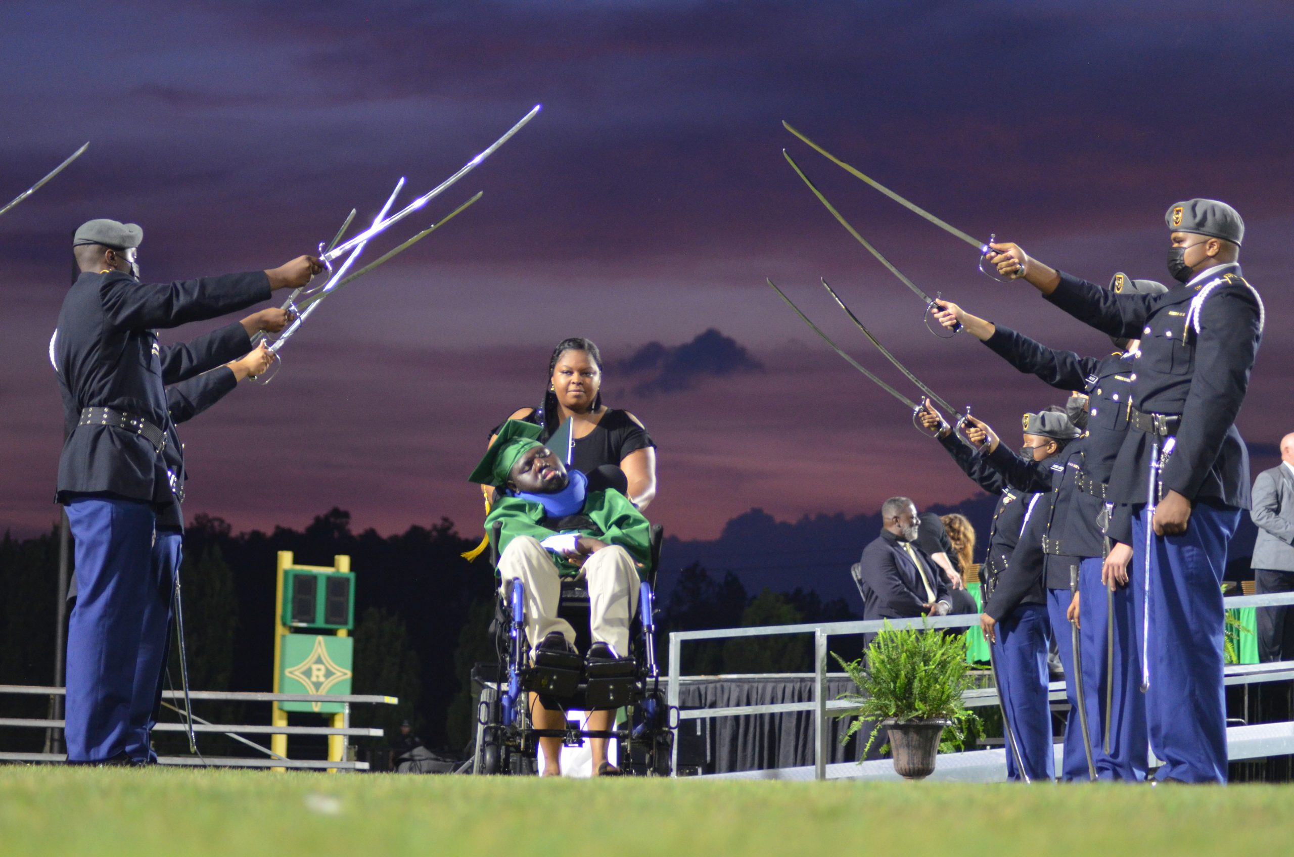 Timothy Bethea, dressed in green cap and gown, is accompanied by teacher Takia York at Richmond Senior High School's Raider Stadium.