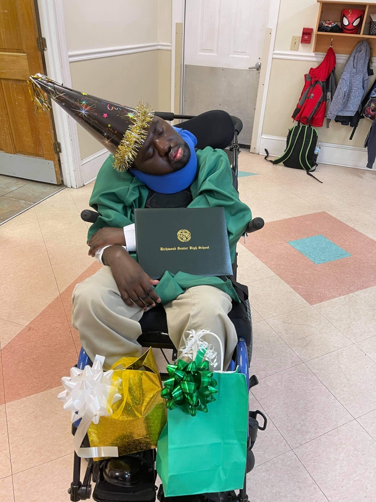 Pence Place resident Timothy Bethea wearing his green high school graduation cap and gown holding his diploma.